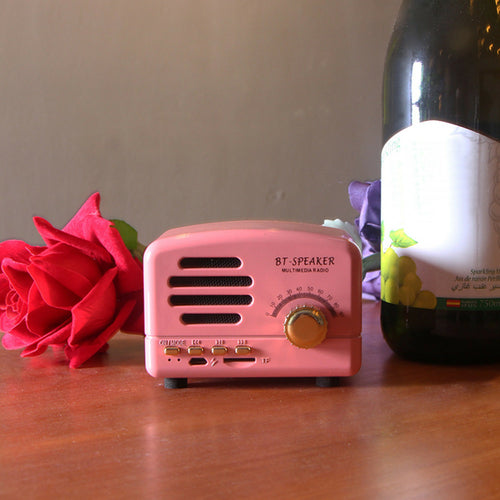 Pink BT-speaker next to a red rose and a bottle on a wooden surface